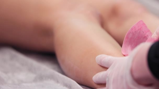 El procedimiento de depilación - el maestro depilando las piernas femeninas usando las rayas rosadas que enceran — Vídeo de stock