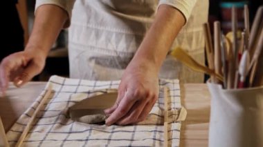 Young woman potter rolling out a piece of clay using a rolling pin