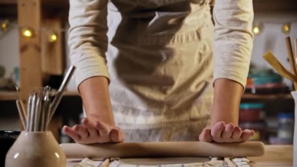 Young woman potter rolling out the clay in flat circle shape using a rolling pin — Vídeos de Stock