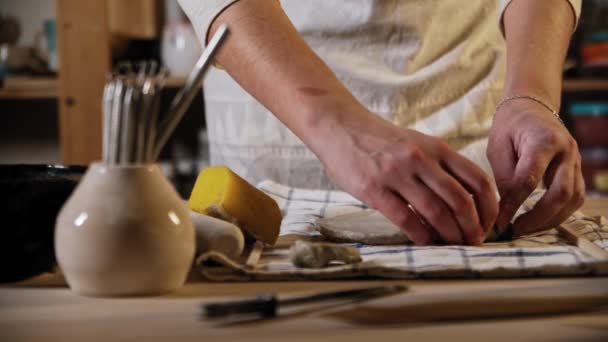 Young woman potter puts small pieces of clay under the big circle part of it — Stock Video