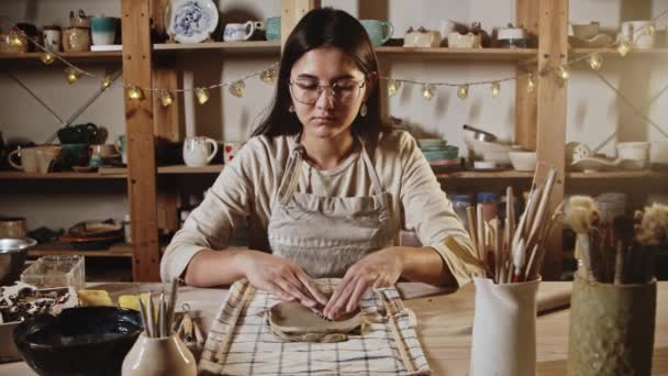 Young woman potter makes patterns of the piece of clay using stamping — Stock video