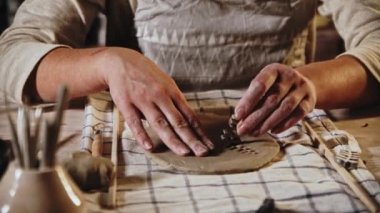 Young woman potter makes a design on the clay plate using a stamp in a leaves shape