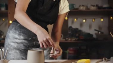 Young woman potter trying on a clay handle to a cup