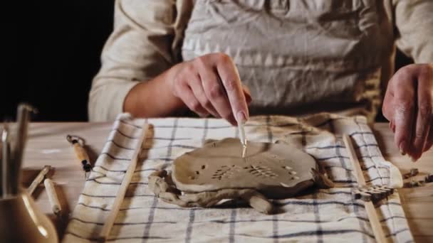 Young woman potter makes patterns on the piece of clay using a tool — 图库视频影像