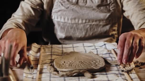 Young woman potter makes patterns on the wet clay plate using a tool — Stock video