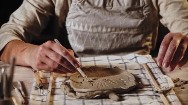 Young woman makes patterns on the wet clay plate using a tool — Stockvideo