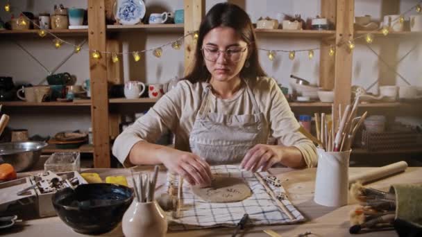 Young woman potter makes a design on the clay plate using a stamp — Stok video