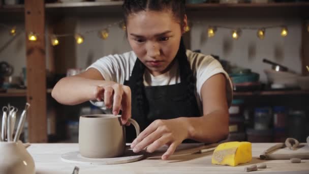 Young woman potter trying on a clay handle to a cup in art studio — Stok video