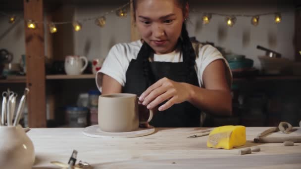 Young woman potter trying on a wet clay handle to a cup — Video