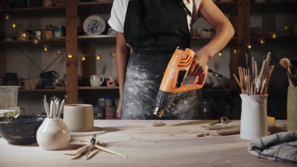 Young woman potter burns clay handle using an industrial dryer — Stok video