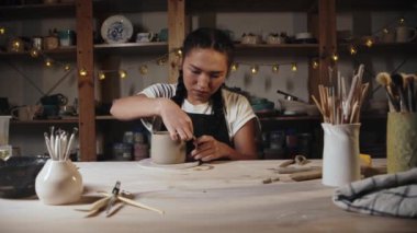 Young woman potter trying on a clay handle to a cup and looking over it