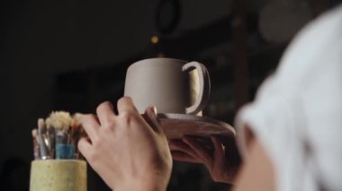 Young woman potter attaching a handle to a clay cup