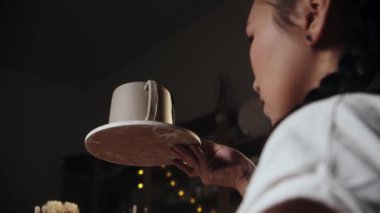 Young woman potter holding a clay cup on the plate and looking at it