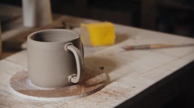 Young woman potter spraying water on the edges of the handle and a cup