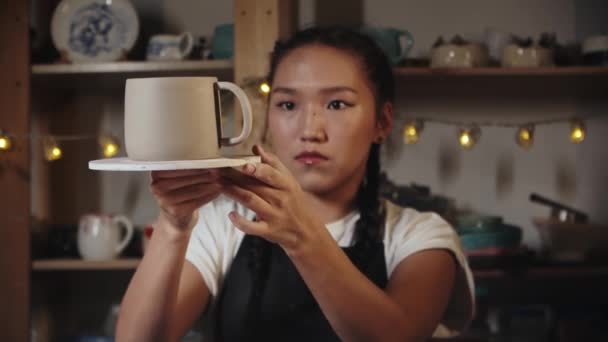 Young woman trying on a clay handle to a cup and looking over it — 비디오