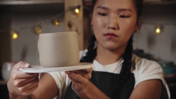 Young woman potter trying on a handle to a finished clay cup — Vídeo de stock