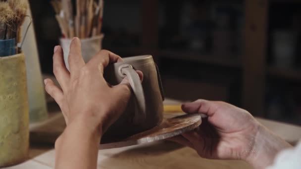 Young woman pressing the piece of clay to an edge of the handle and a cup — Stok video