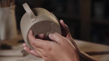 Woman potter chipping away the excess of the clay from the bottom of a cup