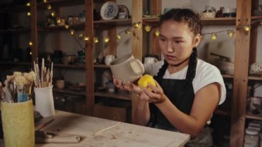 Young woman potter smoothing out the clay cup using a sponge