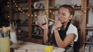Young woman potter smoothing out the clay cup using a wet brush