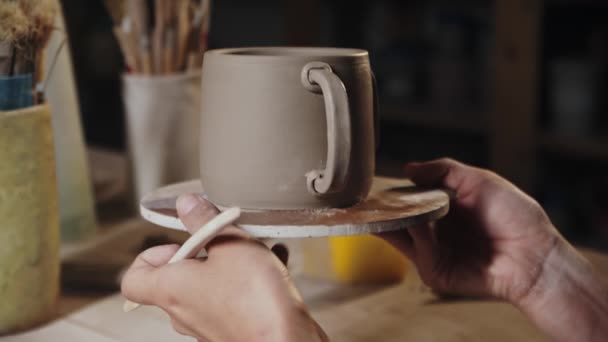Young woman putting on the design to a piece of clay on the edge of the handle and the cup — Stockvideo
