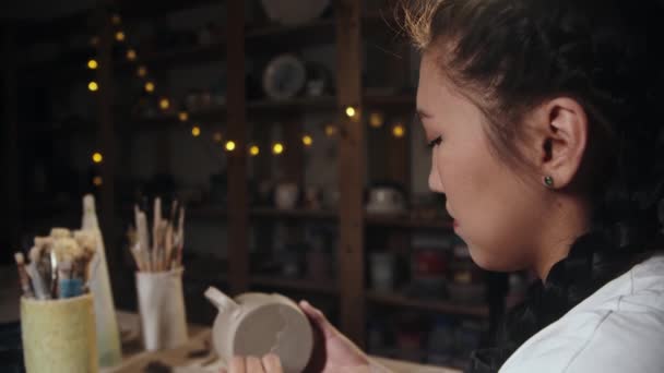 Young woman potter chipping away the excess of the clay from the bottom of a cup — Stockvideo