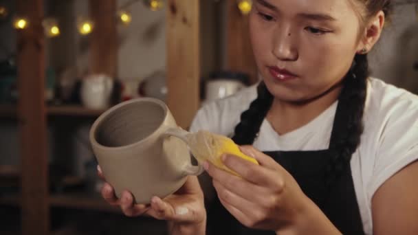 Young woman potter smoothing out the clay cup using a wet sponge — Stockvideo