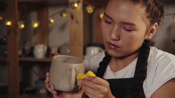 Young asian woman potter smoothing out the clay cup using a yellow wet sponge — Αρχείο Βίντεο