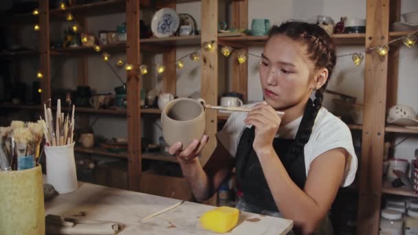 Молода жінка розгладжує глиняну чашку за допомогою вологого пензлика — стокове відео