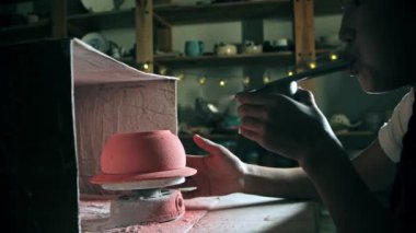 Young woman potter manually sprays the paint by blowing into the device