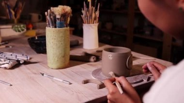 Pottery in the studio - woman potter tries on the handle to the cup and looking at it