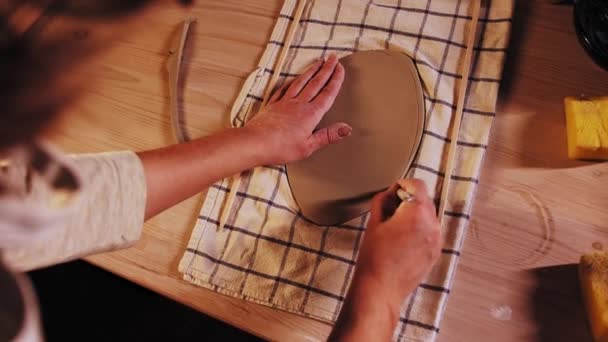 Pottery in the studio - young woman potter cutting off edges of a piece of clay on the table — Stock video