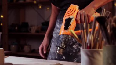 Pottery in the studio - woman potter burns clay handle using an industrial dryer