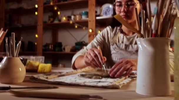 Pottery in the studio - young woman potter makes patterns on a piece of clay — Vídeos de Stock