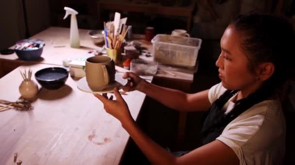 Pottery in the studio - woman potter tries on the handle to the cup and looking at it in warm lighting — 图库视频影像