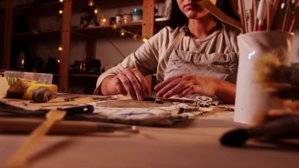 Pottery in the studio - woman potter makes patterns on the piece of clay in warm lighting — Stok video