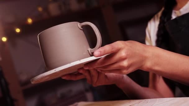 Pottery in the studio - woman potter holding a cup on the plate and starts smearing parts of clay on the joint on the handle and a cup — 图库视频影像