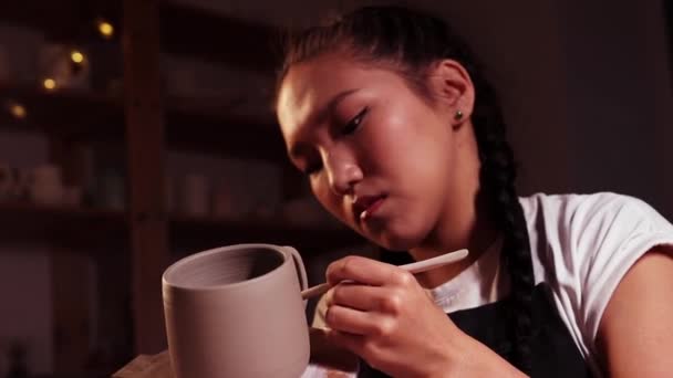 Pottery in the studio - woman holding a cup on the plate and smearing parts of clay on the joint on the handle and a cup — Stok video