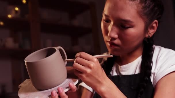 Pottery in the studio - asian woman holding a cup on the plate and smearing parts of clay on the joint on the handle and a cup using a tool — Stok video