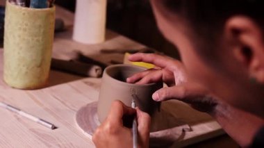Pottery in the art studio - woman potter makes ribs on the cup for next attaching handle to it