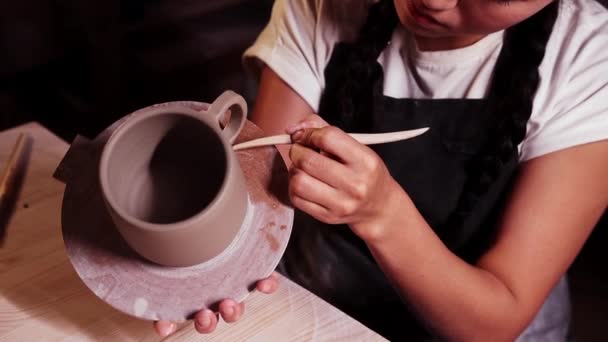 Pottery in the art studio - woman holding a cup on the plate and smearing clay on the joint on the handle and a cup using a tool — Stockvideo