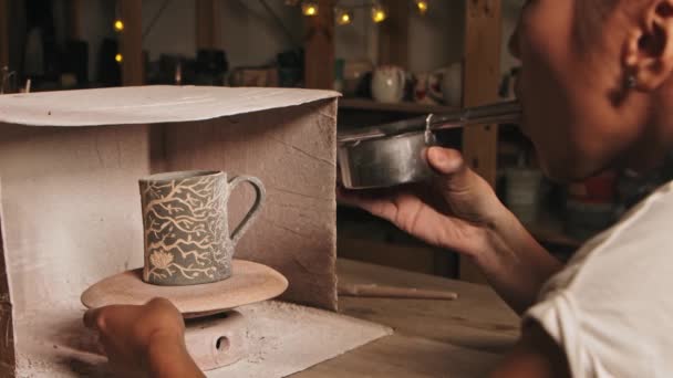 Pottery in the studio - woman potter manually sprays white paint by blowing into the device — Video