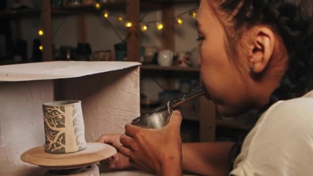 Pottery in the studio - woman potter manually sprays white paint on the clay cup by blowing in the device — Stok video