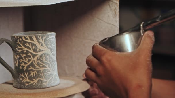 Кераміка в студії - гончар вручну розбризкує білу фарбу на глиняній чашці, продуваючи пристрій — стокове відео