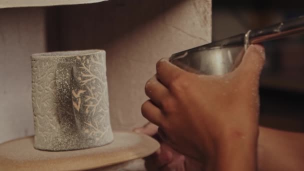 Кераміка в студії - гончар вручну обприскує білий порошок фарбою на глиняній чашці, дме в пристрій — стокове відео