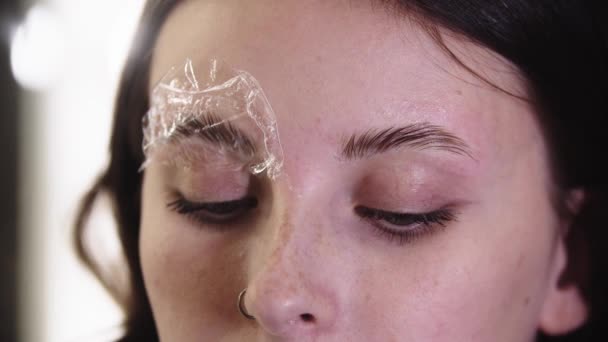 Eyebrow lamination - ένας ειδικός στα φρύδια χτενίζει τις τρίχες των φρυδιών με μια θεραπεία πάνω τους — Αρχείο Βίντεο