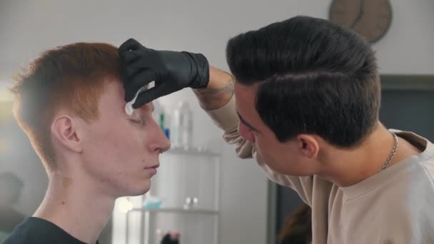Trabalhando com sobrancelhas - um mestre de sobrancelhas homem limpando as sobrancelhas de seu cliente masculino antes do trabalho — Vídeo de Stock