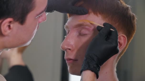 Brow master tillämpa vax på toppen av ögonbrynet på sin manliga klient — Stockvideo