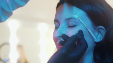 Neon ışıklı çekici bir kadın kaş ağdası yaptırıyor.