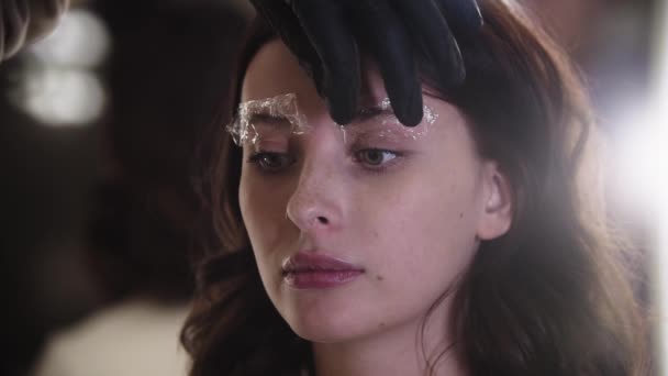 Augenbrauen-Laminierung - Augenbrauen-Spezialist entfernt die Umhüllung auf der Braue seines Kunden und kämmt die Haare mit einer Bürste — Stockvideo